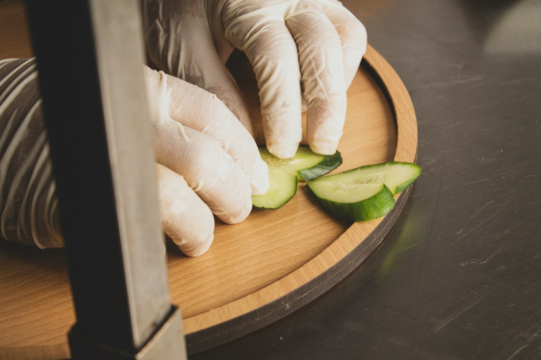 a person in white gloves cutting cucumbers on a cutting board